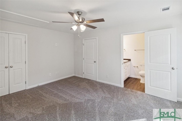 unfurnished bedroom featuring ceiling fan, connected bathroom, a closet, and dark colored carpet