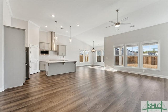 kitchen featuring pendant lighting, dark wood-type flooring, appliances with stainless steel finishes, a center island with sink, and wall chimney exhaust hood