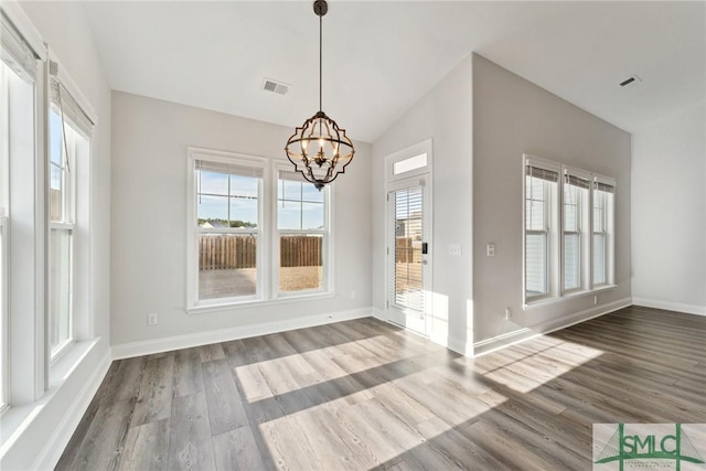 unfurnished dining area featuring hardwood / wood-style floors, vaulted ceiling, and a chandelier