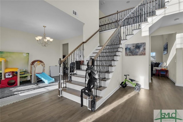 staircase with hardwood / wood-style floors, a towering ceiling, and a chandelier