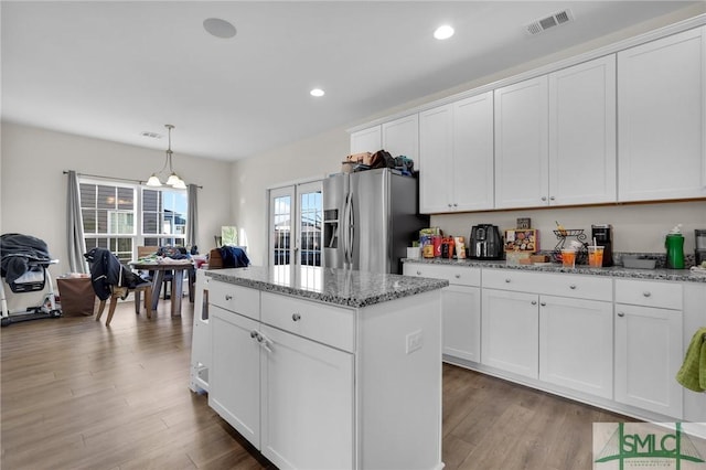 kitchen with pendant lighting, stainless steel fridge, white cabinetry, a center island, and light stone countertops