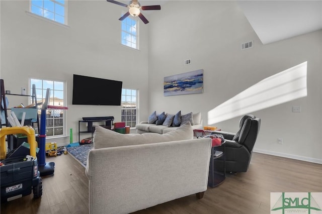 living room with dark wood-type flooring, ceiling fan, and a towering ceiling