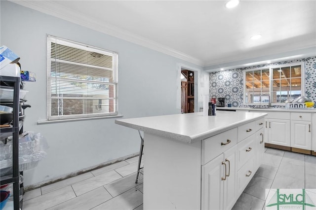 kitchen with sink, a breakfast bar area, ornamental molding, a kitchen island, and white cabinets