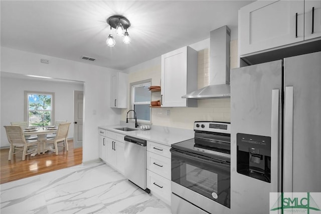 kitchen featuring wall chimney exhaust hood, sink, white cabinetry, appliances with stainless steel finishes, and backsplash