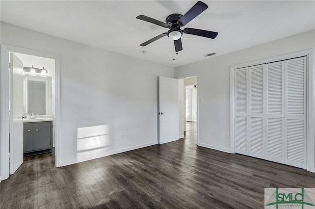 unfurnished bedroom with sink, ensuite bath, dark wood-type flooring, ceiling fan, and a closet