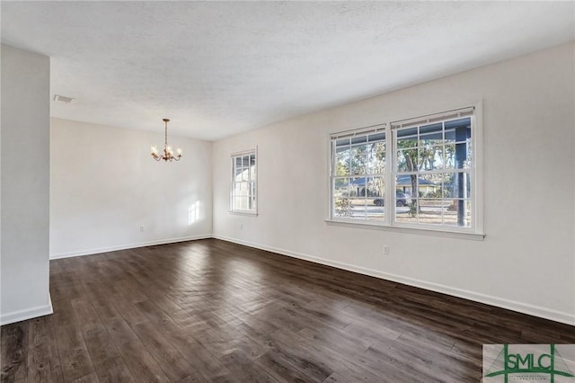 spare room featuring an inviting chandelier, a textured ceiling, and dark hardwood / wood-style flooring