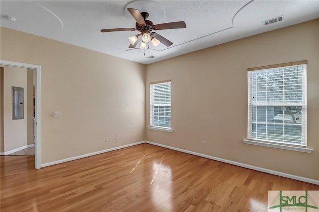 unfurnished room with a textured ceiling, electric panel, ceiling fan, and light wood-type flooring