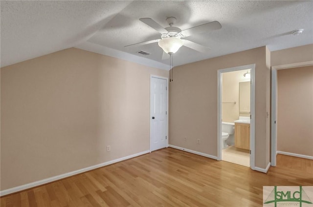 unfurnished bedroom featuring lofted ceiling, a textured ceiling, light wood-type flooring, and ensuite bath