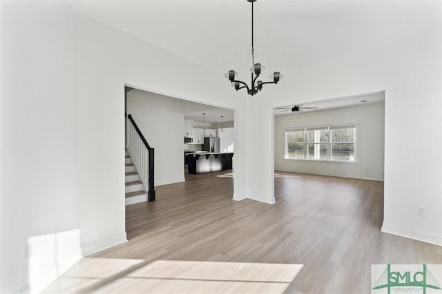 unfurnished living room featuring hardwood / wood-style flooring and ceiling fan with notable chandelier