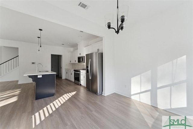 kitchen featuring appliances with stainless steel finishes, decorative light fixtures, white cabinetry, a breakfast bar area, and a kitchen island with sink