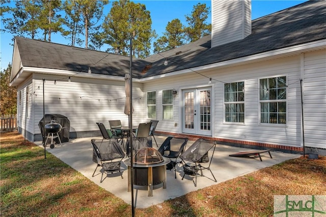 rear view of house featuring a patio, a lawn, french doors, and an outdoor fire pit