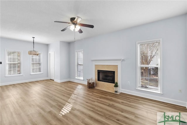 unfurnished living room with a tile fireplace, a wealth of natural light, hardwood / wood-style floors, and ceiling fan