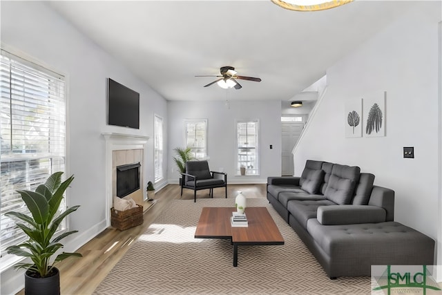 living room featuring a tiled fireplace, light hardwood / wood-style flooring, and ceiling fan