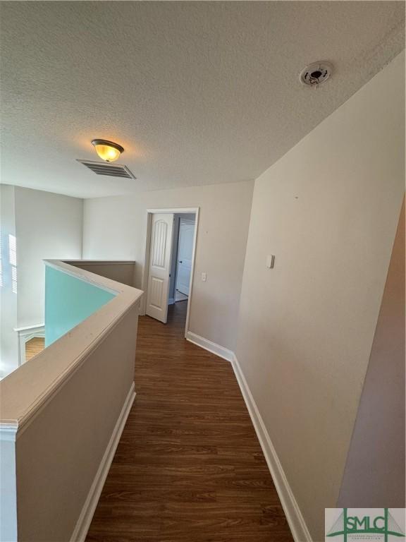 709 Eden Ln, Hinesville, GA 31313 - hallway featuring a textured ceiling, baseboards, dark wood-style flooring, and an upstairs landing