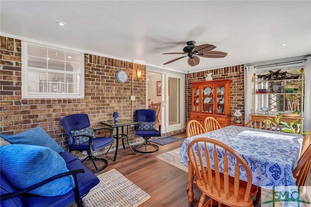 dining area with ceiling fan, brick wall, and wood-type flooring