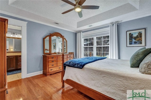 bedroom featuring ensuite bathroom, ornamental molding, a textured ceiling, a raised ceiling, and light wood-type flooring