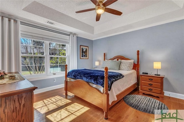 bedroom featuring a raised ceiling, wood-type flooring, ceiling fan, and a textured ceiling