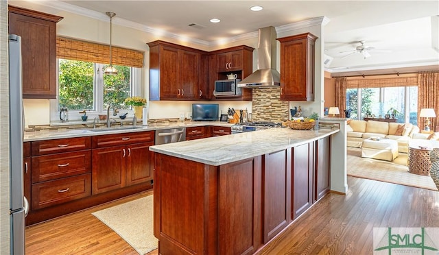 kitchen with pendant lighting, sink, appliances with stainless steel finishes, light stone countertops, and wall chimney exhaust hood