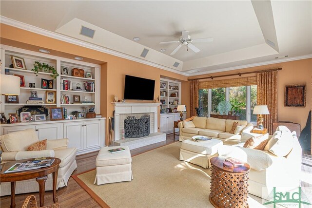 living room with hardwood / wood-style flooring, built in features, ceiling fan, a tray ceiling, and ornamental molding