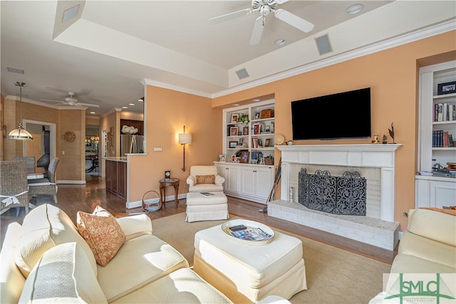 living room featuring ornamental molding, hardwood / wood-style floors, built in features, and a tray ceiling