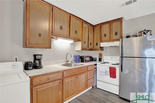 kitchen with stainless steel refrigerator, washer / dryer, sink, white electric range oven, and light wood-type flooring