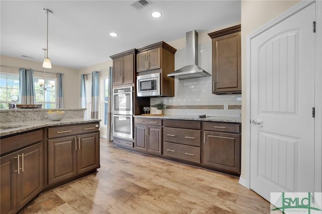 kitchen with appliances with stainless steel finishes, hanging light fixtures, dark brown cabinetry, tasteful backsplash, and wall chimney exhaust hood