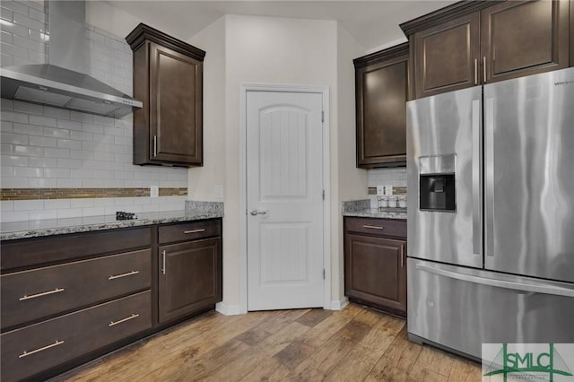 kitchen with light stone countertops, stainless steel fridge with ice dispenser, light hardwood / wood-style flooring, and wall chimney range hood