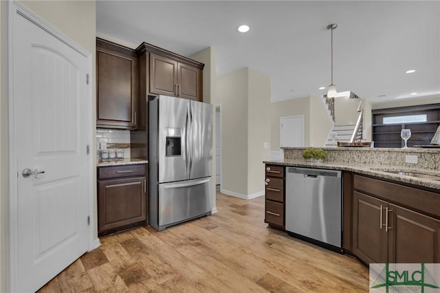 kitchen with tasteful backsplash, light hardwood / wood-style floors, stainless steel appliances, light stone countertops, and dark brown cabinets