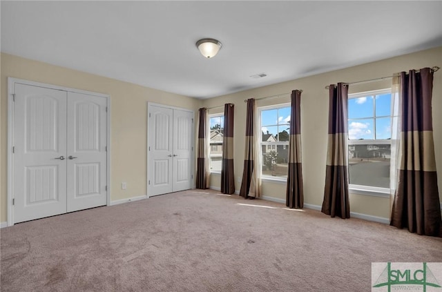 unfurnished bedroom featuring two closets and light colored carpet