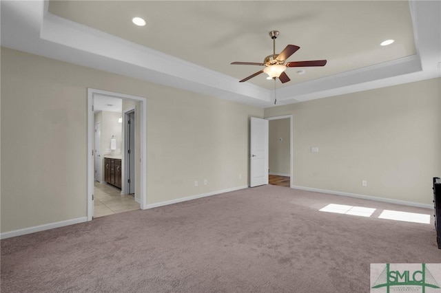 unfurnished room with a tray ceiling, light colored carpet, and ceiling fan