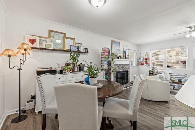 dining space with ceiling fan, wood-type flooring, a fireplace, and ornamental molding