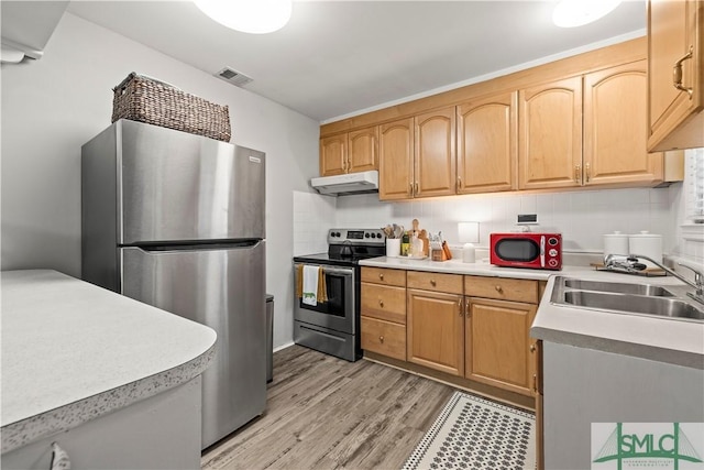 kitchen with appliances with stainless steel finishes, light brown cabinetry, sink, backsplash, and light hardwood / wood-style floors