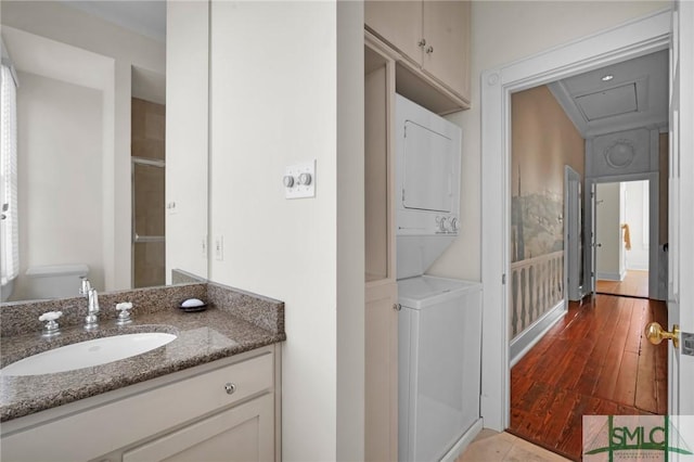 bathroom featuring vanity, stacked washer / drying machine, wood-type flooring, and toilet