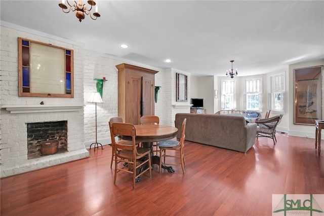 dining space featuring an inviting chandelier, a fireplace, wood-type flooring, and brick wall