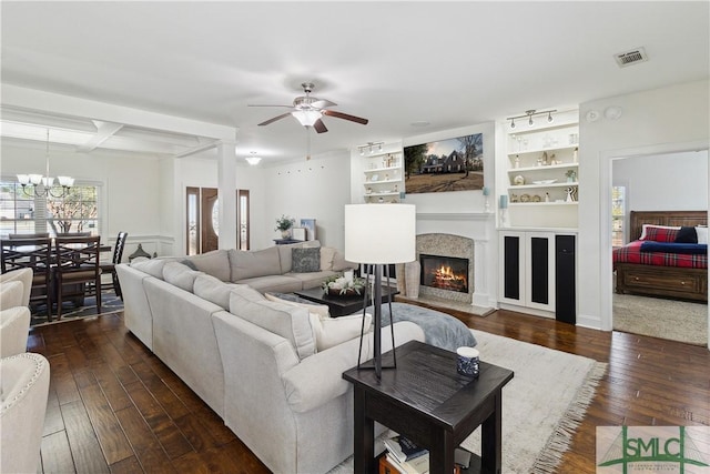 living room featuring dark hardwood / wood-style flooring, built in features, a high end fireplace, beam ceiling, and ceiling fan with notable chandelier