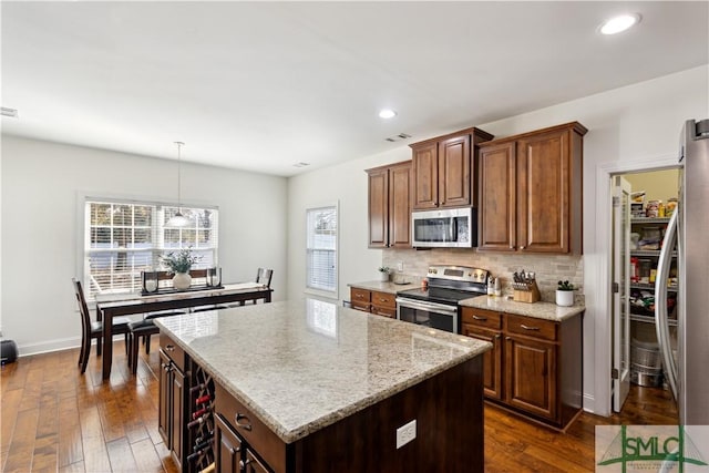 kitchen featuring tasteful backsplash, decorative light fixtures, a center island, appliances with stainless steel finishes, and dark hardwood / wood-style flooring