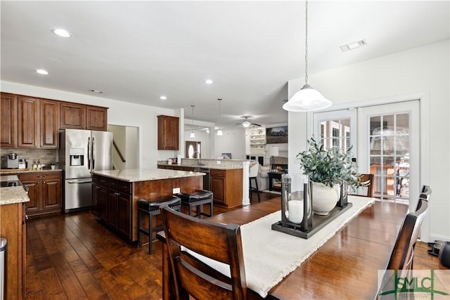 kitchen featuring stainless steel refrigerator with ice dispenser, dark wood-type flooring, light stone counters, decorative light fixtures, and a kitchen island