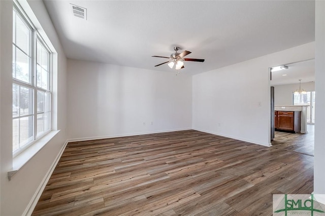 empty room with a healthy amount of sunlight, ceiling fan with notable chandelier, and wood-type flooring