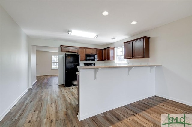 kitchen with light hardwood / wood-style flooring, kitchen peninsula, a breakfast bar area, and black appliances