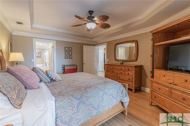 bedroom with crown molding, ensuite bath, ceiling fan, light hardwood / wood-style floors, and a raised ceiling