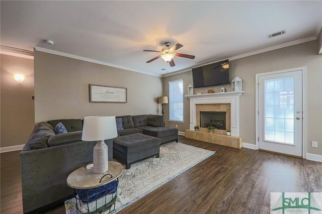 living room with a tiled fireplace, ornamental molding, ceiling fan, and dark hardwood / wood-style flooring