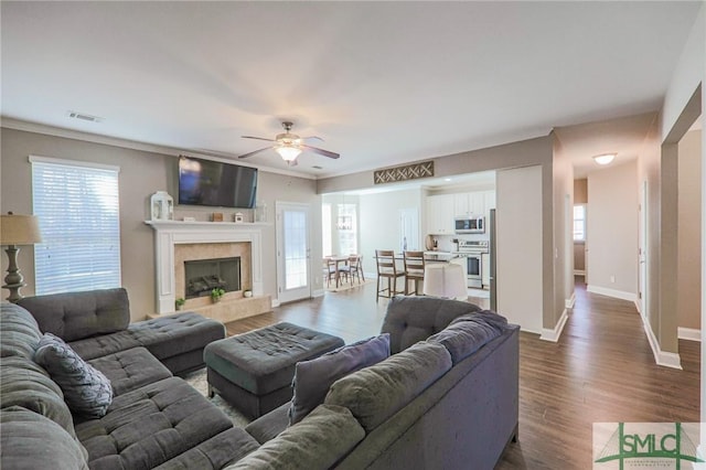 living room featuring crown molding, a tile fireplace, dark hardwood / wood-style floors, and a healthy amount of sunlight