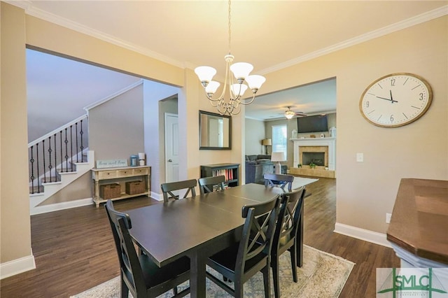 dining space with a tiled fireplace, ornamental molding, dark wood-type flooring, and ceiling fan with notable chandelier