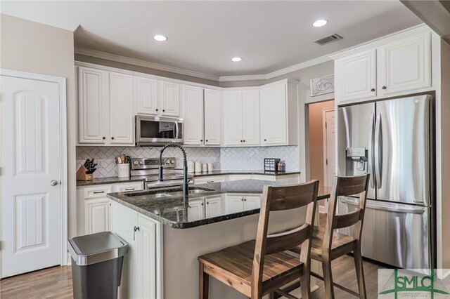 kitchen with white cabinetry, a kitchen breakfast bar, stainless steel appliances, light hardwood / wood-style floors, and dark stone counters