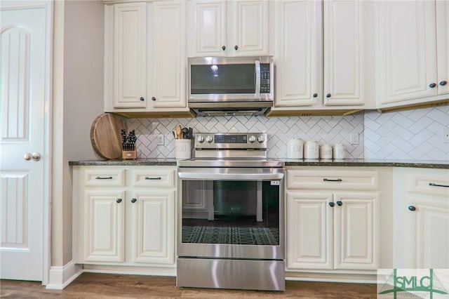 kitchen with dark wood-type flooring, dark stone countertops, white cabinetry, stainless steel appliances, and tasteful backsplash