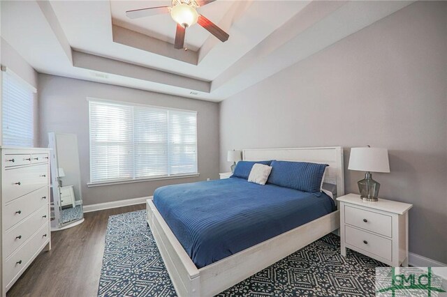 bedroom with ceiling fan, dark hardwood / wood-style floors, and a raised ceiling