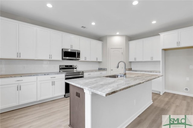 kitchen with stainless steel appliances, white cabinetry, a sink, and an island with sink