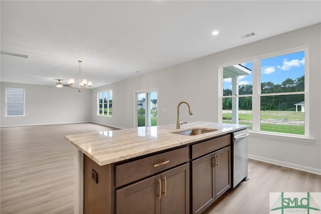 kitchen with light stone counters, a sink, visible vents, stainless steel dishwasher, and a center island with sink