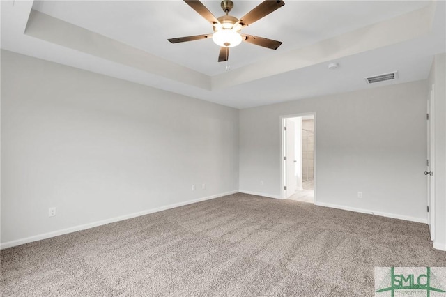 empty room with a tray ceiling, visible vents, a ceiling fan, carpet flooring, and baseboards