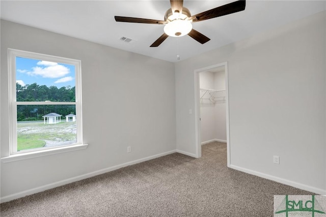 unfurnished bedroom with a ceiling fan, visible vents, baseboards, carpet, and a walk in closet